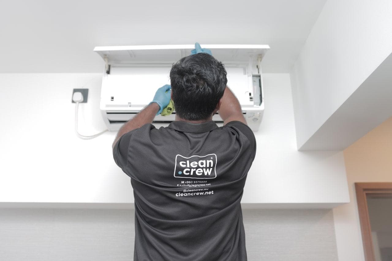 Clean Crew technician cleaning inside a wall-mounted air conditioning unit