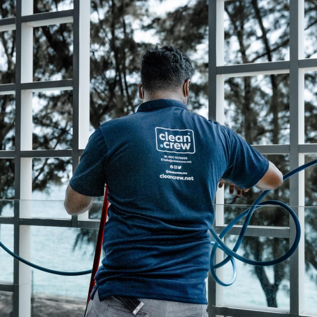 Clean Crew technician rinsing beachfront glass with a hose