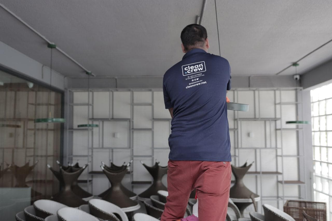 Clean Crew technician dusting pendant lights in a café