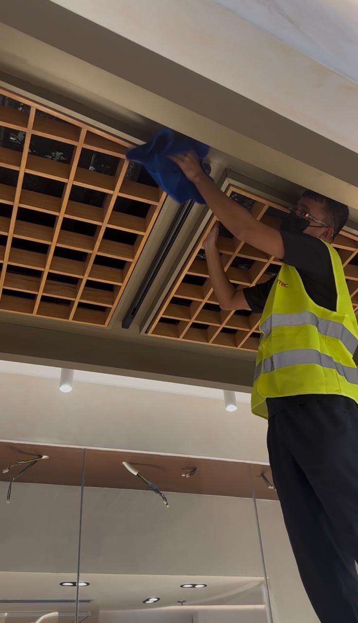 Clean Crew technician in hi-vis cleaning a timber ceiling grid on a fit-out