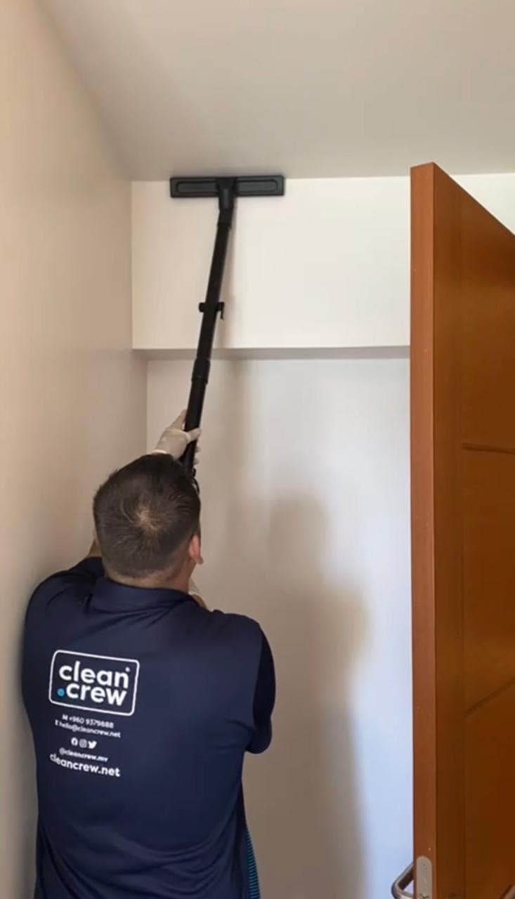Clean Crew technician dusting high on a wall with an extension pole