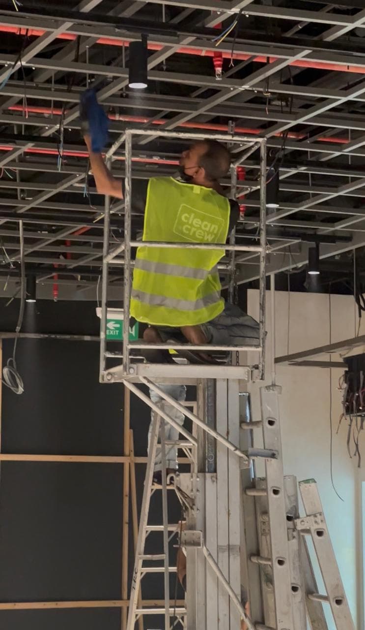 Clean Crew technician on a scaffold tower cleaning an open ceiling grid on a fit-out site