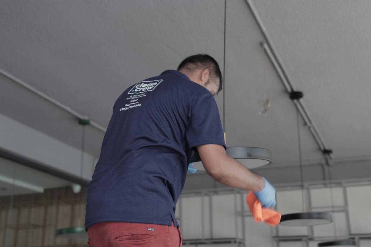 Clean Crew technician dusting ceiling light fittings in a restaurant
