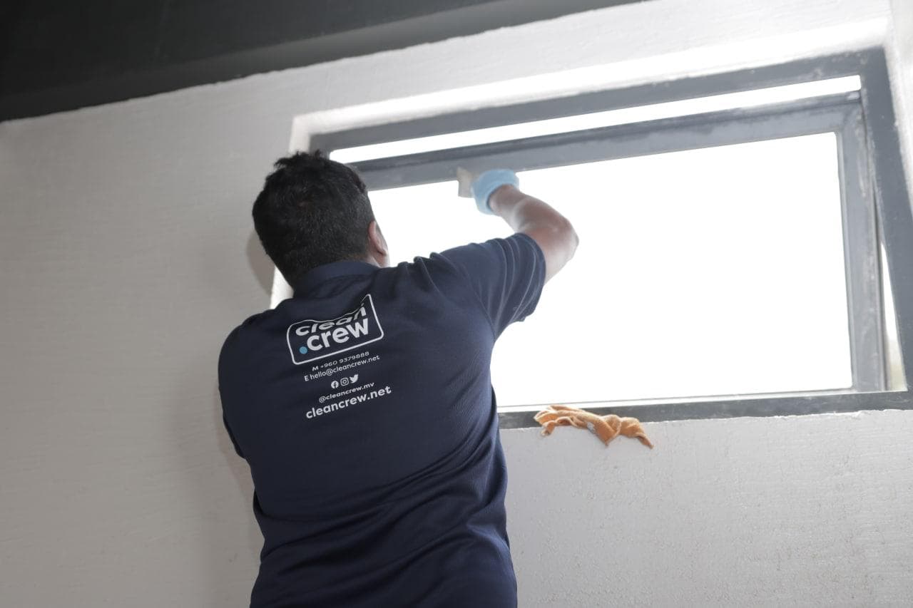 Clean Crew technician cleaning a window frame and glass